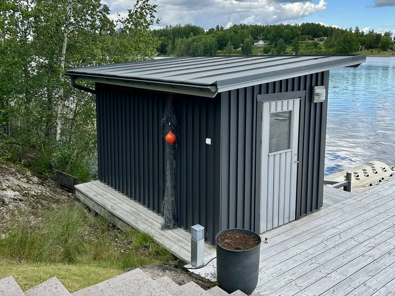 Sjöbod vid sjön i Linköping med nymålad mörkgrå träfasad och ljusgrå vindskivor